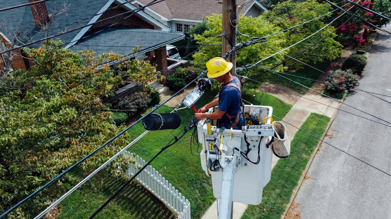 services-01 Electrician in a bucket lift repairing power lines from a utility pole in a suburban neighborhood.