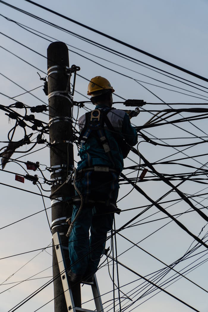 Silhouette of electrician fixing tangled wires on a utility pole in Ubud, Bali at dusk.