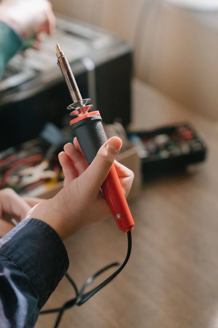 Hand holding a soldering iron ready for electronic repair or assembly.