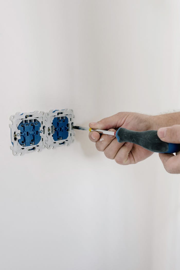 who-we-are Close-up of hands using a screwdriver to install electrical sockets on a white wall.
